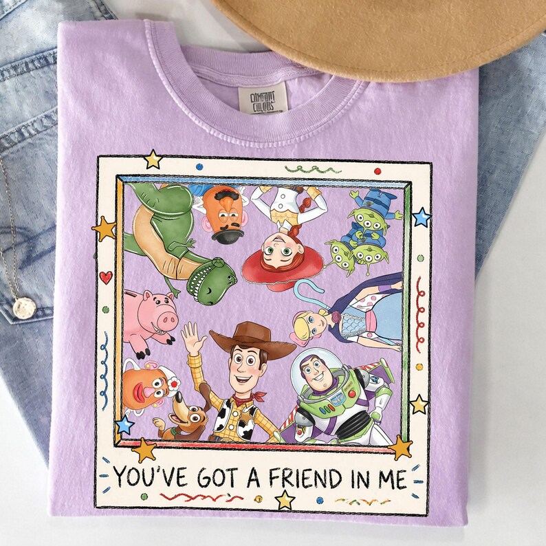 Puede incluir: Una camiseta lila con un dise&ntilde;o enmarcado de personajes de Toy Story, incluyendo a Woody y Buzz Lightyear. El dise&ntilde;o est&aacute; rodeado de estrellas. El texto "YOU'VE GOT A FRIEND IN ME" est&aacute; impreso debajo.