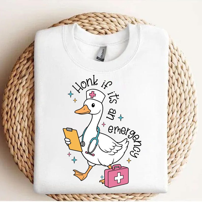 Puede incluir: Camiseta blanca con un ganso de dibujos animados que lleva un gorro de enfermera y sostiene un portapapeles. El texto "Honk if it's an emergency" est&aacute; escrito alrededor del ganso.
