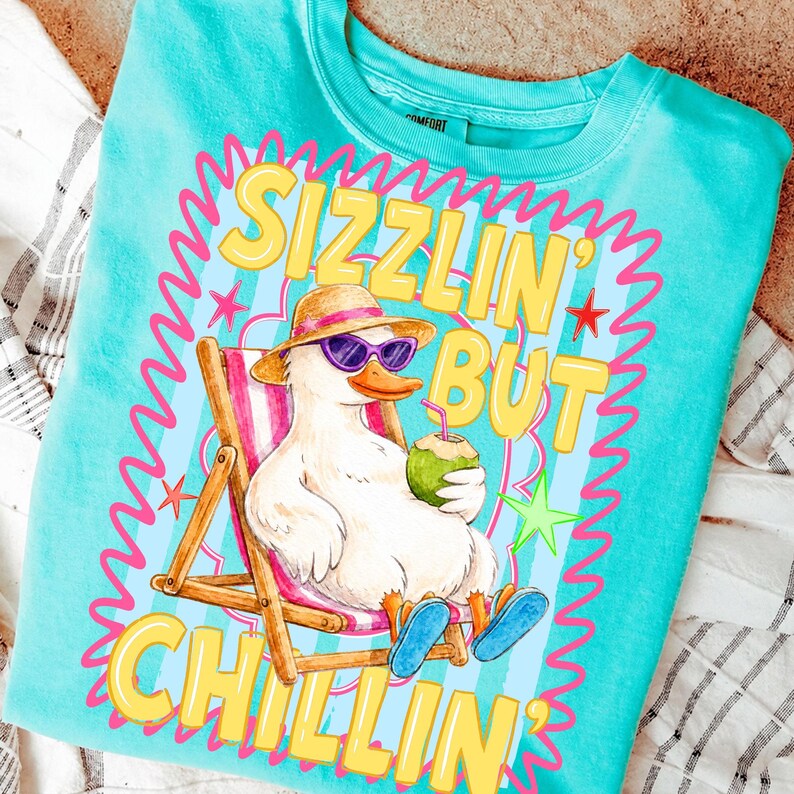 May include: Turquoise crew neck sweatshirt with a graphic of a duck wearing sunglasses and a hat, relaxing in a beach chair while holding a coconut drink. The text reads "Sizzlin' But Chillin'" in yellow and pink.