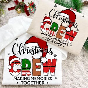 Może przedstawiać: Dwie świąteczne bluzy, jedna biała i jedna beżowa. Obie mają napis "Christmas CREW" w świątecznym wzorze z czapkami Świętego Mikołaja i akcentami płatków śniegu. Fraza "MAKING MEMORIES TOGETHER" jest również zawarta.