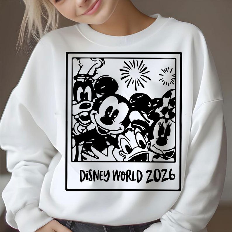 Op de afbeelding: Witte sweatshirt met een zwart-wit afbeelding van Disney-personages, waaronder Mickey Mouse, Minnie Mouse en Donald Duck. De afbeelding is omlijst met de tekst "DISNEY WORLD 2026".