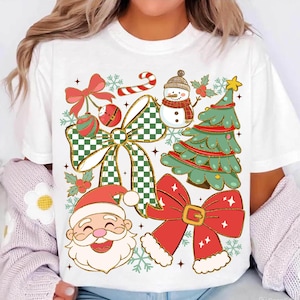 May include: White t-shirt featuring a festive Christmas design. The graphic includes a snowman, Santa Claus, a Christmas tree, bows, ornaments, and snowflakes. The design incorporates red, green, gold, and white colors, creating a cheerful holiday theme.