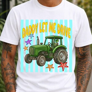 Pu&ograve; includere: T-shirt bianca con grafica di un trattore verde e la scritta "DADDY LET ME DRIVE" in giallo. Il design include stelle blu, viola e rosse, su uno sfondo a righe azzurre.