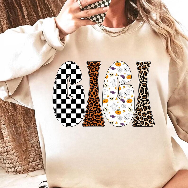 May include: A beige sweatshirt with the word "GIGI" in a retro font. The letters have different patterns: a black and white checkerboard, leopard print, and a Halloween-themed pattern with ghosts and pumpkins.