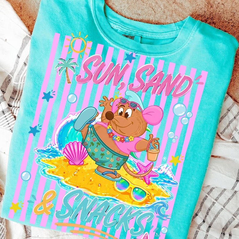May include: Turquoise crew neck t-shirt with a graphic featuring a cartoon mouse on a beach. The design includes the words "Sun, Sand & Snacks" in pink and blue, along with beach-themed illustrations like a palm tree, sun, and seashells.