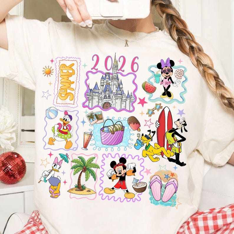 May include: Cream-colored t-shirt featuring colorful cartoon illustrations of Disney characters, including Mickey and Minnie Mouse, Donald Duck, and Goofy. The design includes the word "SUMMER" and the number "2026".