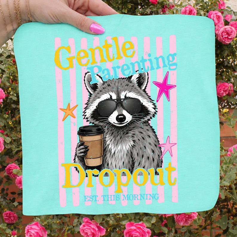 Op de afbeelding: Een turquoise draagtas met een wasbeer met een zonnebril en een koffiekopje. De tas heeft de woorden "Gentle Parenting Dropout" in gele en roze tekst, met steraccenten en roze strepen.