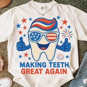 May include: White t-shirt with a patriotic tooth graphic wearing sunglasses with the American flag design. The tooth has blue arms giving a thumbs up, surrounded by red and blue stars and fireworks. The text "MAKING TEETH GREAT AGAIN" is printed below.