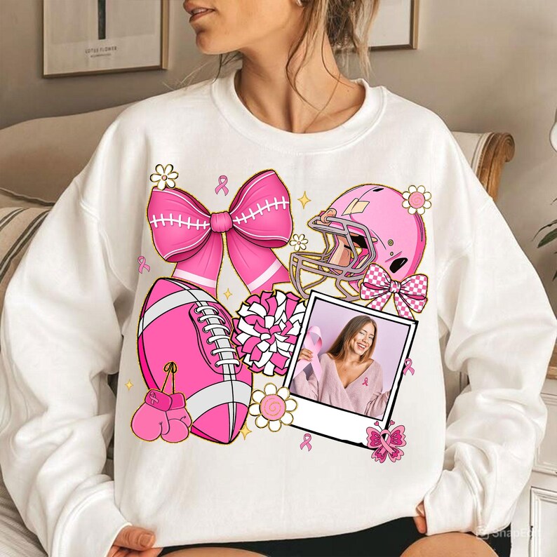 May include: White sweatshirt with a pink football, helmet, boxing gloves, and bow graphic. A photo of a woman holding a pink ribbon is also featured. The design includes pink flowers and ribbons.