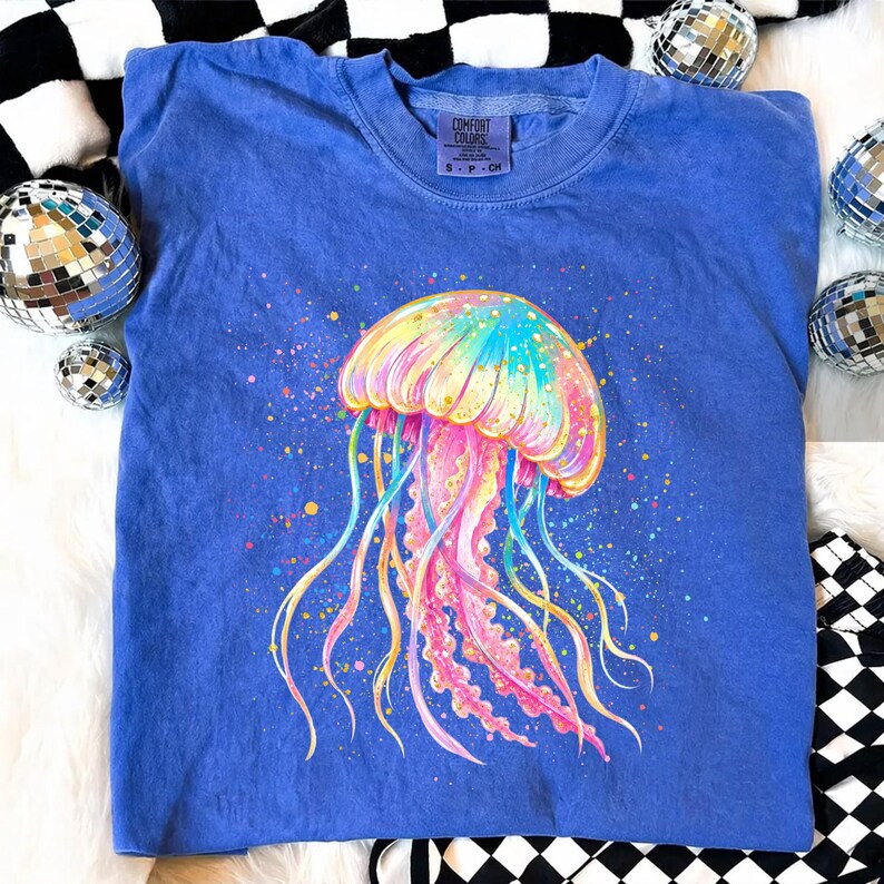 May include: A blue Comfort Colors sweatshirt featuring a colorful jellyfish design. The jellyfish is depicted with a rainbow of colors, including pink, yellow, blue, and green. The sweatshirt has a crew neck and the Comfort Colors logo is visible.