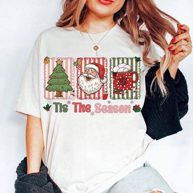 Puede incluir: Camiseta blanca con un dise&ntilde;o navide&ntilde;o festivo. El gr&aacute;fico incluye un &aacute;rbol de Navidad, Pap&aacute; Noel y una taza de chocolate caliente, todo dentro de marcos decorativos. El texto "Tis The Season" est&aacute; impreso debajo.