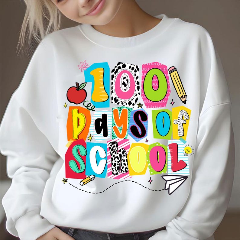 May include: White sweatshirt with a colorful graphic that reads "100 Days of School." The design includes an apple, pencil, and paper airplane. The text is in various bright colors and patterns, perfect for celebrating a school milestone.