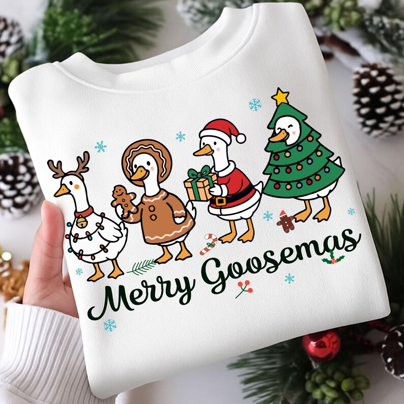 Peut inclure: Sweat-shirt blanc avec un motif festif repr&eacute;sentant des oies de dessin anim&eacute; v&ecirc;tues de tenues de f&ecirc;te. Une oie porte des bois de renne, une autre tient un bonhomme en pain d'&eacute;pices, et d'autres sont en costumes de P&egrave;re No&euml;l et de sapin de No&euml;l. Le texte "Merry Goosmas" est imprim&eacute; en dessous.