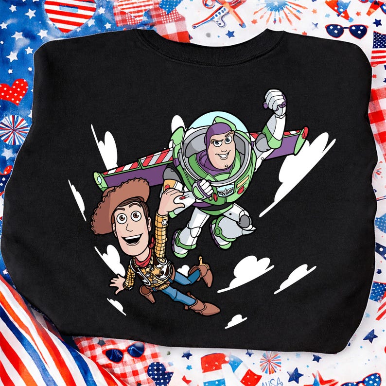 Puede incluir: Sudadera negra con una ilustraci&oacute;n de dibujos animados de Woody y Buzz Lightyear en el aire. Woody lleva un sombrero de vaquero y Buzz un traje espacial verde y blanco. Nubes blancas en el fondo.
