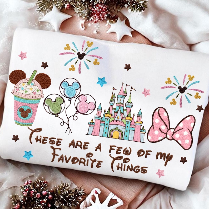 May include: White sweatshirt with colorful embroidered Disney-themed graphics. Features a castle, balloons, a drink, fireworks, and a bow. Text reads "These are a few of my favorite things."