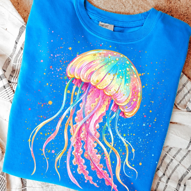 May include: A blue sweatshirt featuring a colorful jellyfish design. The jellyfish is depicted with a rainbow-colored bell and long, flowing tentacles in shades of pink, yellow, and blue. Splatter details add to the artistic look.