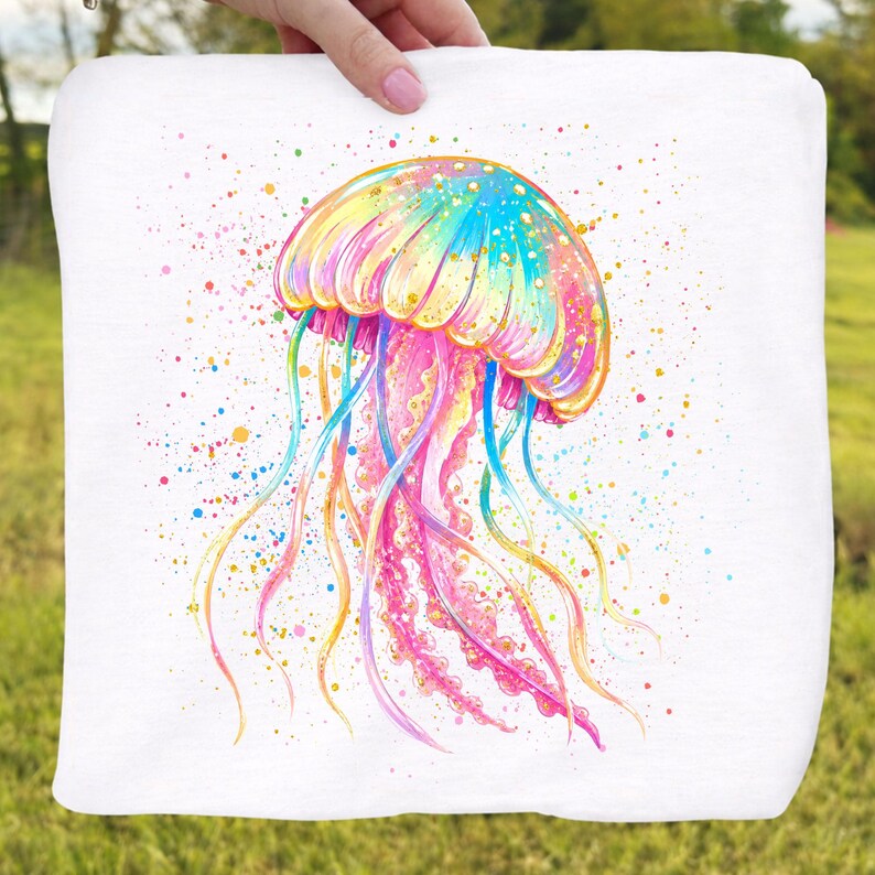 May include: A white square pillow with a watercolor painting of a colorful jellyfish. The jellyfish is depicted in shades of pink, yellow, blue, and green, with long, flowing tentacles and colorful paint splatters.