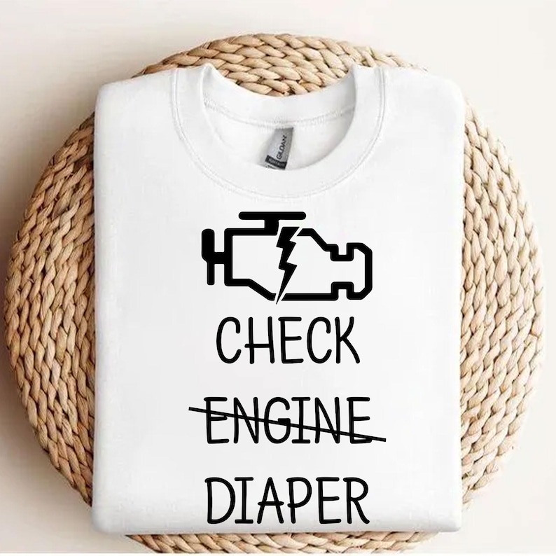 May include: White t-shirt with a black check engine light icon and the text "CHECK ENGINE" crossed out and "DIAPER" below it.