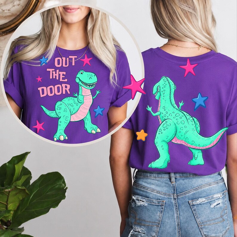 Może przedstawiać: Fioletowa koszulka z turkusową grafiką dinozaura i napisem "OUT THE DOOR". Dinozaur ma r&oacute;żowe akcenty i jest otoczony r&oacute;żowymi, niebieskimi i ż&oacute;łtymi gwiazdami. Tył koszulki r&oacute;wnież posiada grafikę dinozaura i gwiazdy.