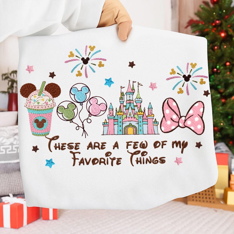 May include: White fabric with embroidered Disney-themed designs. Features a castle, balloons, fireworks, a bow, and a drink, with the text "These are a few of my favorite things". The design includes Mickey Mouse silhouettes and stars.