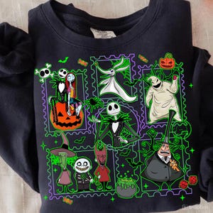 May include: Black sweatshirt featuring a colorful graphic of characters from The Nightmare Before Christmas. The design includes Jack Skellington, Sally, Zero, and Oogie Boogie, with a green and purple border.