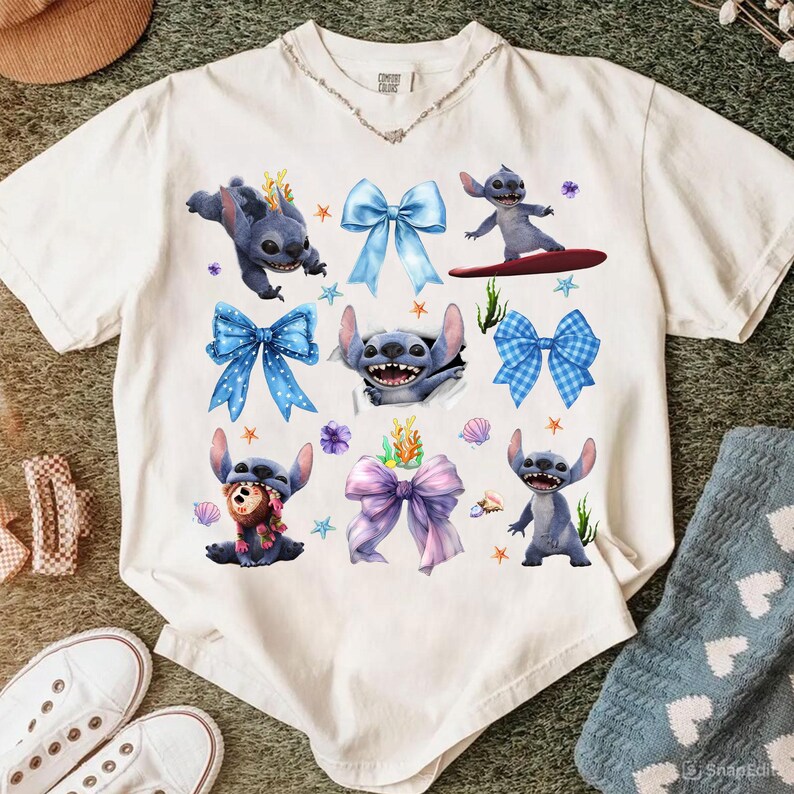 May include: White t-shirt featuring a collage of Stitch illustrations and colorful bows. The design includes Stitch in various poses, surrounded by blue, purple, and pink bows, starfish, and floral accents. The shirt has a crew neck and short sleeves.