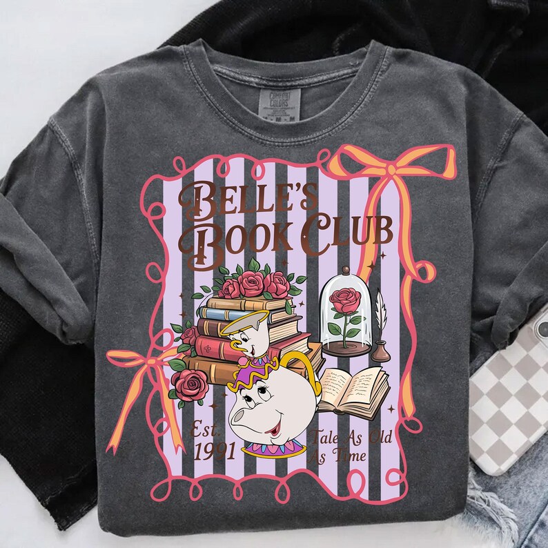 May include: Dark grey sweatshirt with a graphic design. The design includes the text "BELLE'S BOOK CLUB", books, roses, and a teapot. A rose is in a glass dome, with the phrase "Tale As Old As Time" below.