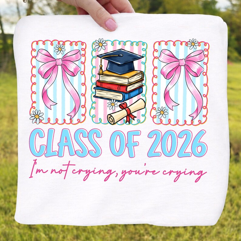May include: White graduation-themed fabric with the text "CLASS OF 2026" in light blue. The design includes pink bows, daisies, and a graduation cap on books. The phrase "I'm not crying, you're crying" is also included.