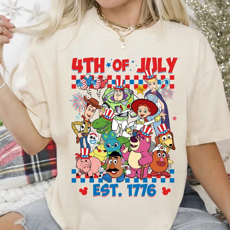 May include: A white t-shirt with a graphic of Toy Story characters celebrating the 4th of July. The text "4th of July Est. 1776" is printed on the shirt.