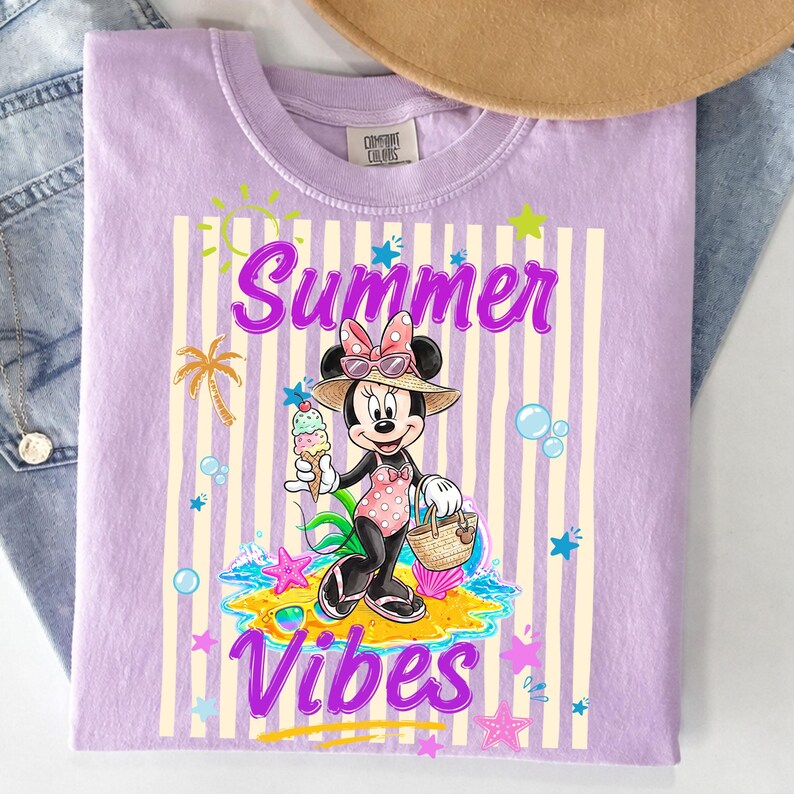 Może przedstawiać: Liliowa koszulka Comfort Colors z grafiką Myszki Minnie w stroju kąpielowym, trzymającej lody i koszyk. Napis "Summer Vibes" jest napisany zabawną czcionką, z paskowanym tłem i letnimi ilustracjami.