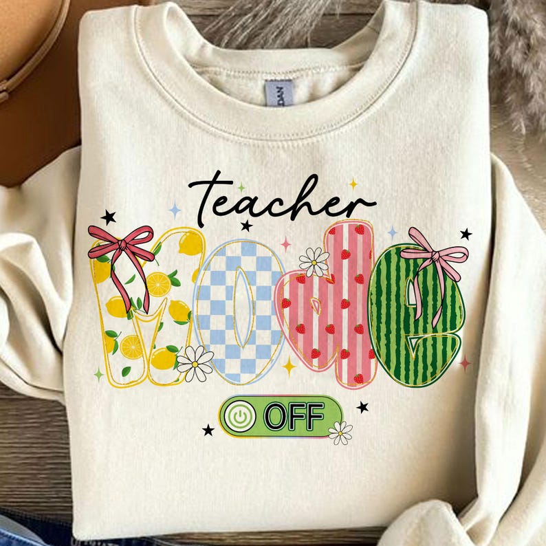 Op de afbeelding: Cr&egrave;mekleurige sweatshirt met de woorden "Teacher" en "WOE OFF" in een speels, kleurrijk ontwerp. De letters zijn versierd met citroenen, ruitpatronen, aardbeien en watermeloen. Geaccentueerd met strikken, bloemen en sterren.