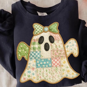 May include: Navy blue sweatshirt featuring a patchwork ghost design. The ghost has a green and white checkered bow, black oval eyes, and a body composed of floral and patterned fabric squares. The design is outlined with a gold-colored trim.