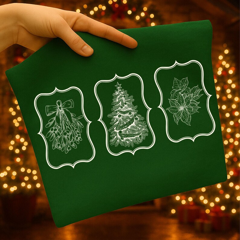 May include: A dark green fabric with three white framed illustrations: mistletoe, a Christmas tree, and a poinsettia. The fabric is held by a hand, with a blurred background of Christmas lights.