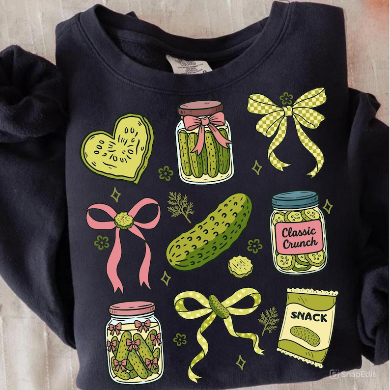 May include: Navy blue sweatshirt featuring a variety of pickle-themed illustrations. The design includes jars of pickles, a pickle heart, a pickle snack bag, and decorative bows. The illustrations are in shades of green, pink, and yellow.