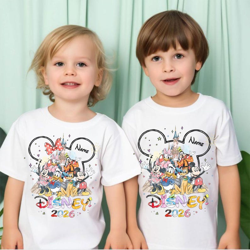 May include: Two white t-shirts with a colorful Disney graphic featuring Mickey Mouse, Minnie Mouse, Donald Duck, and other characters. The shirts have a Mickey Mouse ear outline with the word "Name" and the year "2026".