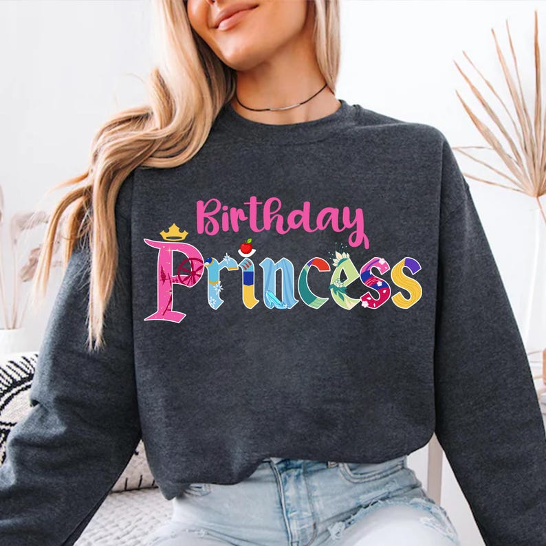 May include: A dark gray sweatshirt with the text "Birthday Princess" in pink lettering. The word "Princess" is made up of colorful images of Disney princesses.
