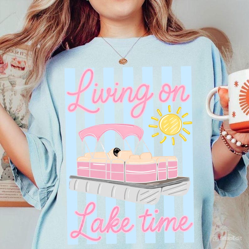 May include: Light blue sweatshirt with a pink and yellow graphic of a pontoon boat, sun, and the words "Living on Lake time" in pink script. The shirt has vertical blue stripes.
