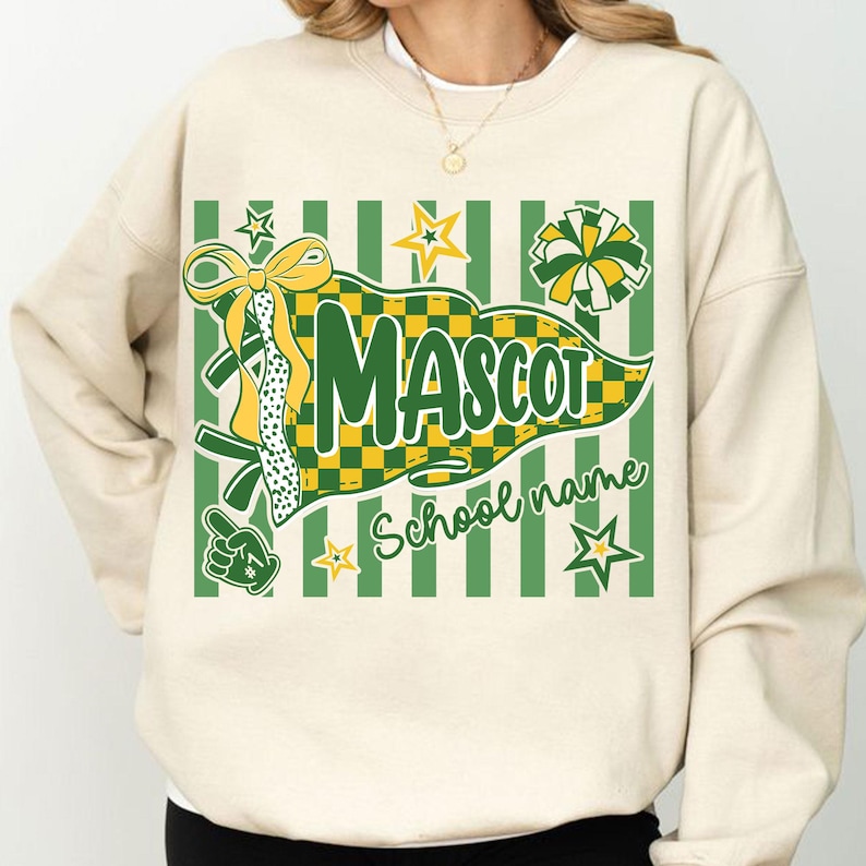 May include: A cream-colored crewneck sweatshirt featuring a graphic print of a green and yellow checkered pennant with the text "MASCOT" and "School name". The design includes a yellow bow, a pom-pom, stars, and a foam finger in green and yellow.
