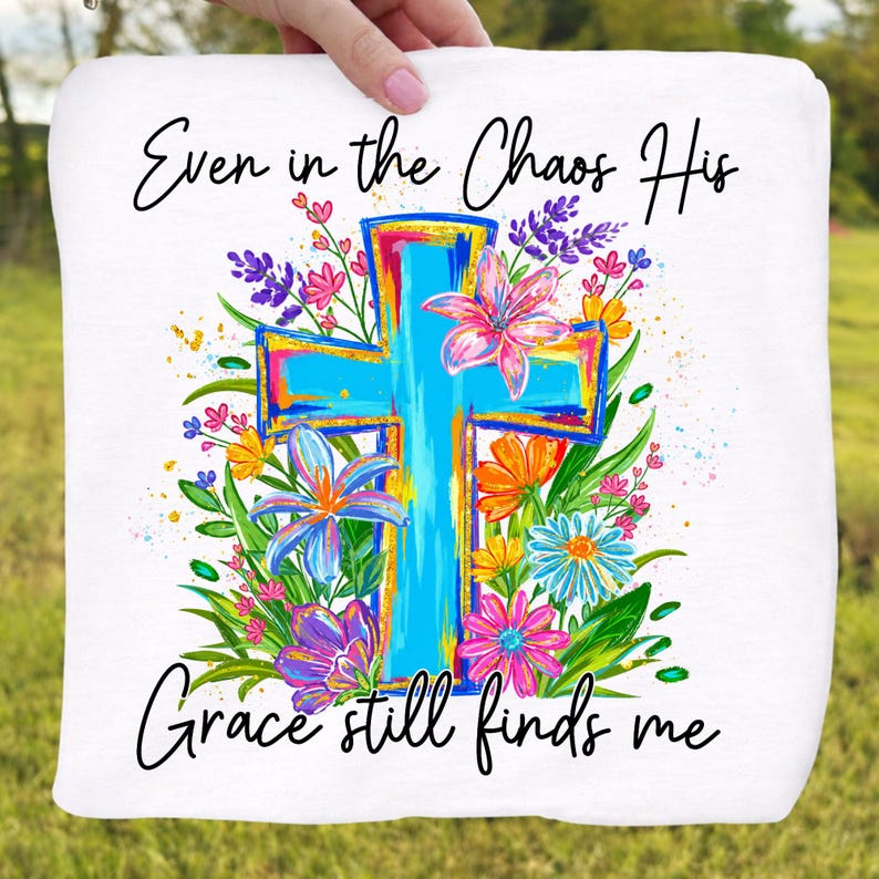 May include: White square fabric with a vibrant, turquoise cross design, surrounded by colorful flowers in pink, purple, orange, and blue. The text reads "Even in the Chaos His Grace still finds me."