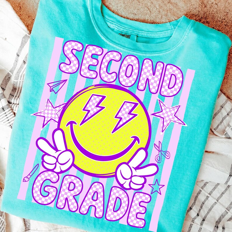 May include: A turquoise sweatshirt with a graphic design for second grade. The design includes a yellow smiley face with purple lightning bolts, peace signs, and the words "SECOND GRADE" in a checkered pattern.