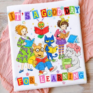 Puede incluir: Una superficie de tela blanca con una ilustraci&oacute;n colorida de varios personajes de libros leyendo. El texto IT'S A GOOD DAY FOR LEARNING est&aacute; impreso en letras de bloque multicolores en la parte superior e inferior.
