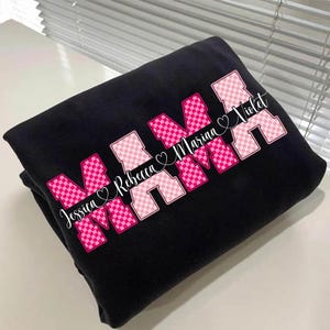 May include: Black sweatshirt with the word "MAMA" in pink and white checkered letters. The names "Jessica Rebecca Marina Violet" are printed in white script across the design. A heart symbol is between each name.