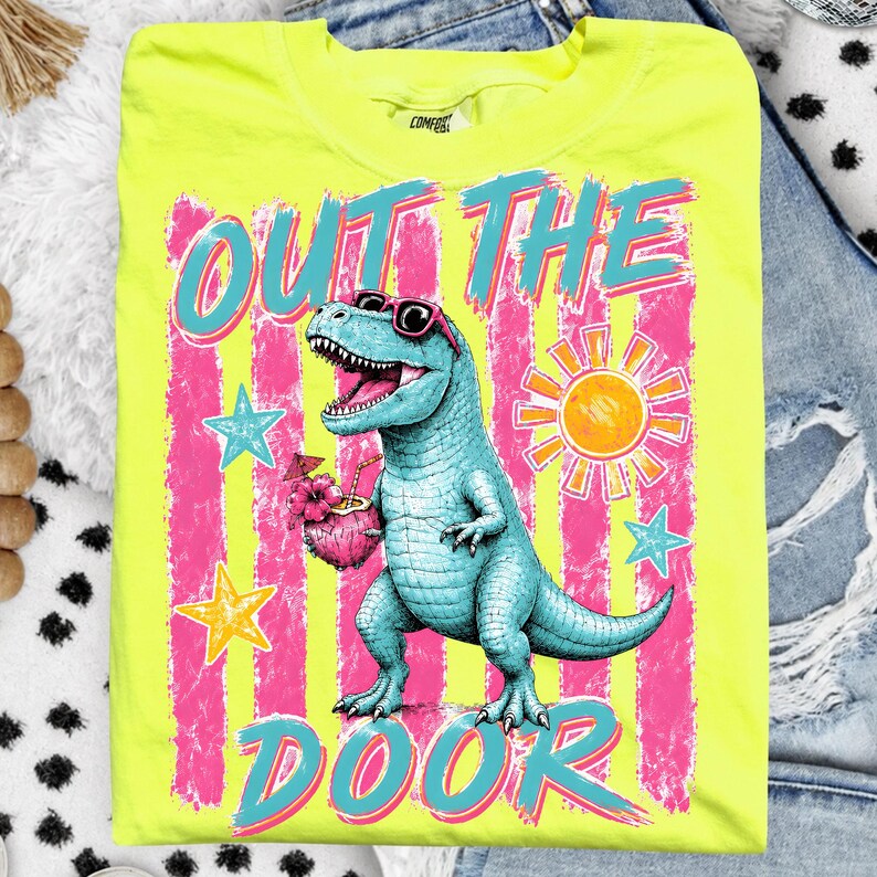 May include: A bright yellow t-shirt featuring a turquoise dinosaur wearing sunglasses and holding a cocktail. The text "OUT THE DOOR" is in turquoise and pink. The design includes pink and white stripes and stars.