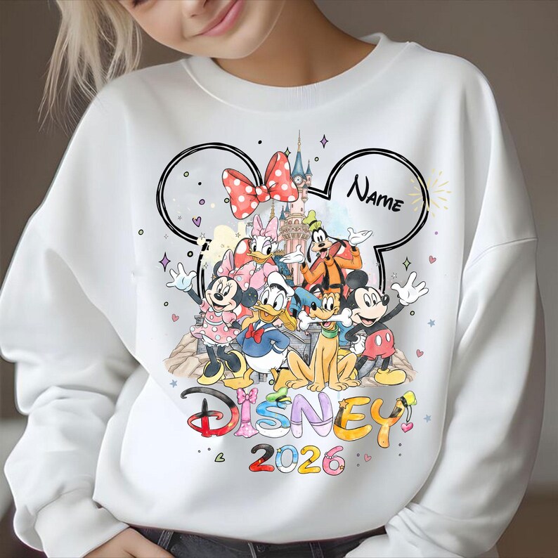 May include: White sweatshirt featuring a Disney design with Mickey Mouse, Minnie Mouse, Donald Duck, and other characters. The design includes a castle, a red polka dot bow, and the text "Disney 2026". A space is available for a name.