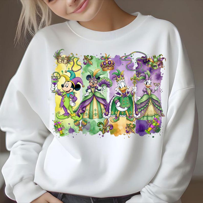 May include: White sweatshirt featuring a colorful graphic of Mickey Mouse, Minnie Mouse, Donald Duck, and Daisy Duck in Mardi Gras attire. The characters are dressed in purple, green, and gold costumes, with masks and crowns. The design includes fleur-de-lis and watercolor effects.