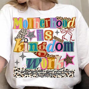 Pu&ograve; includere: T-shirt bianca con la scritta "Motherhood is Kingdom Work" in testo colorato e stratificato. Il design include stelle, fiori e un motivo leopardato. &Egrave; stampato anche il testo "She is strong and dignified... Proverbi 31:25-27".