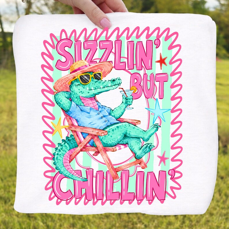 May include: White square towel with a cartoon alligator wearing sunglasses and a straw hat, relaxing in a beach chair and holding a cocktail. The text reads "Sizzlin' But Chillin'" in pink and green.