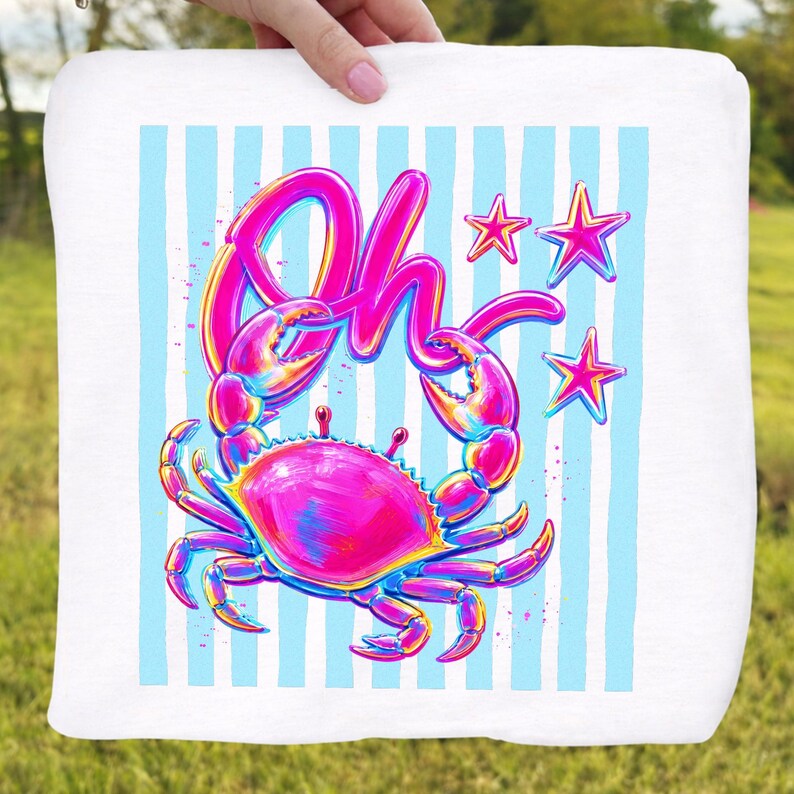 May include: White square towel featuring a vibrant crab illustration with the word "Oh" in a playful font. The crab is in shades of pink, blue, and yellow, set against a backdrop of light blue vertical stripes and pink stars. The towel is held by a person.