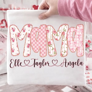 May include: White t-shirt with the word "Mama" in large, decorative letters. The letters are filled with floral, checkered, and bow patterns. Below the word "Mama" are the names Elle, Taylor, and Angela.