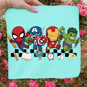 May include: A light blue t-shirt featuring cartoon versions of Spider-Man, Captain America, Iron Man, and the Hulk, each holding a pencil. The design includes school-themed elements like a globe, book, and clock.